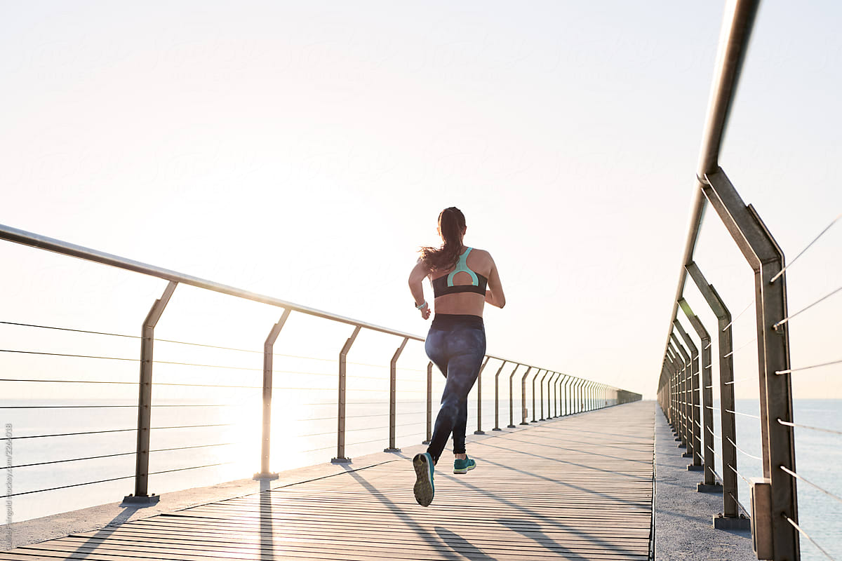 Athletic woman running on pier in sunlight