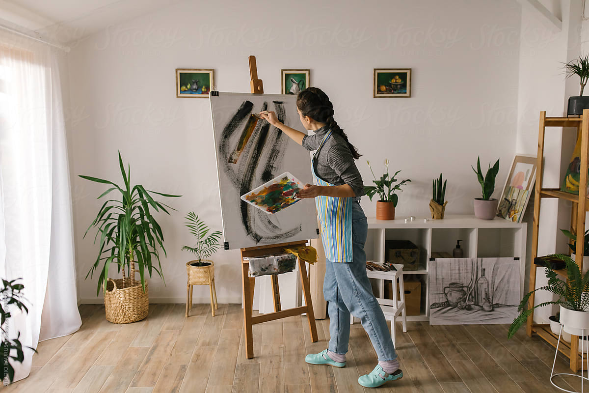 Young artistic woman painting on canvas in art studio