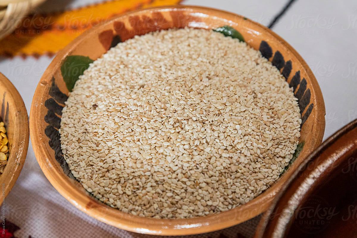 Clay bowl filled with sesame seeds on a table with a white tablecloth