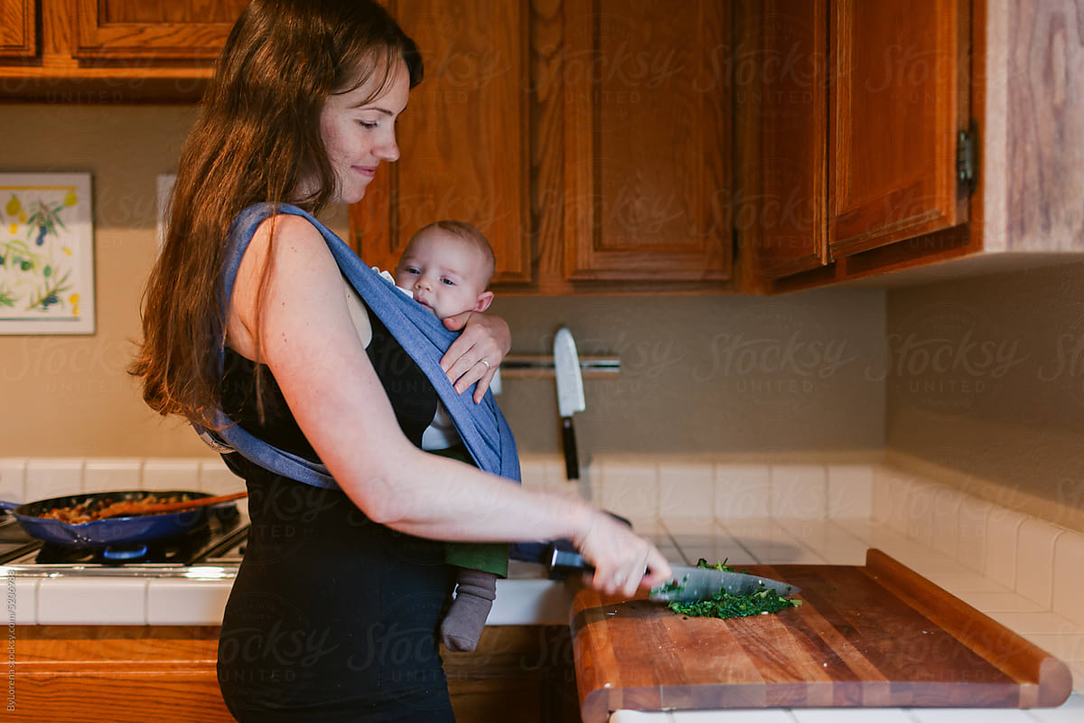 New mom choping celery while carrying her baby
