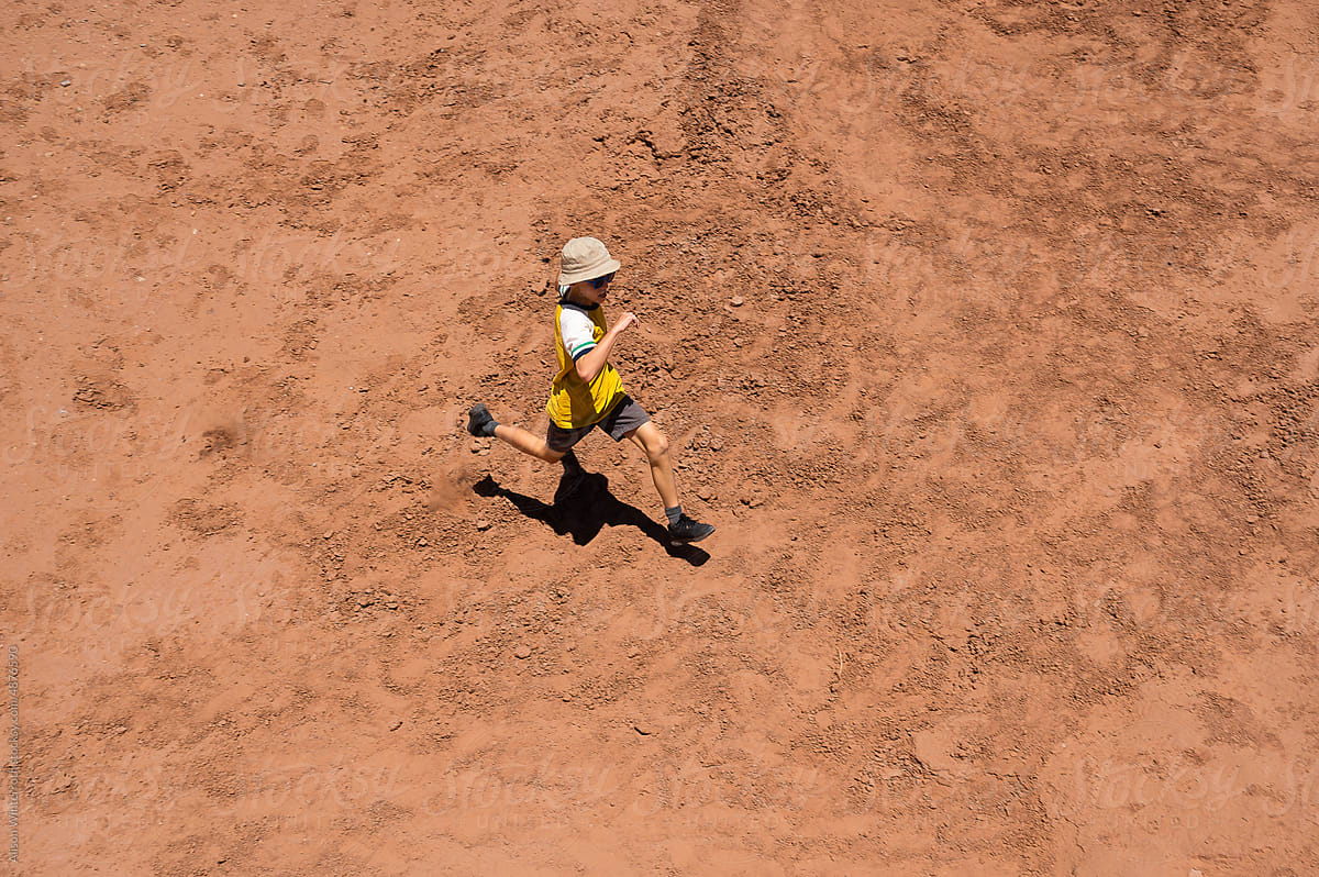 Boy running on red clay from above
