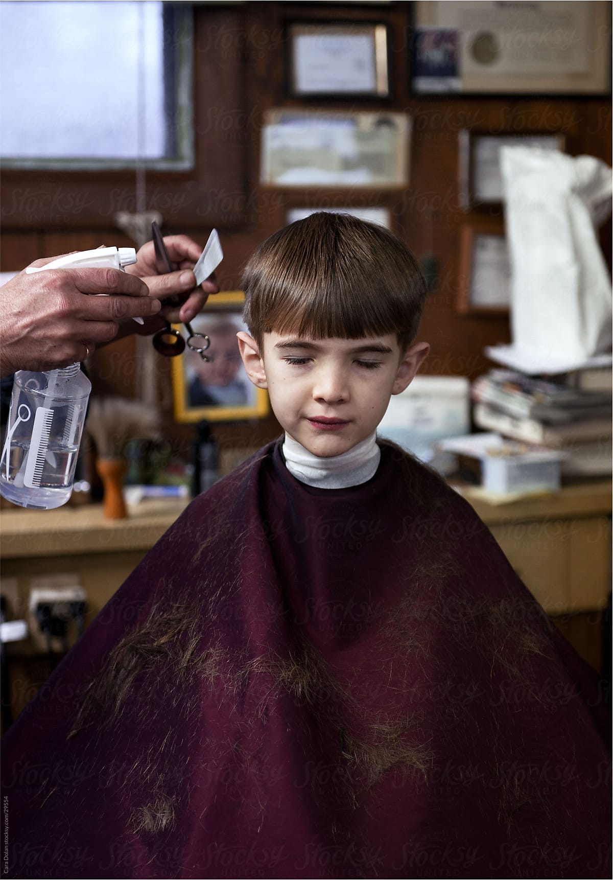 Boy sits quietly in barber\'s chair as he gets his hair cut