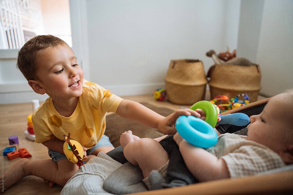 Boy giving colorful toy to baby in room