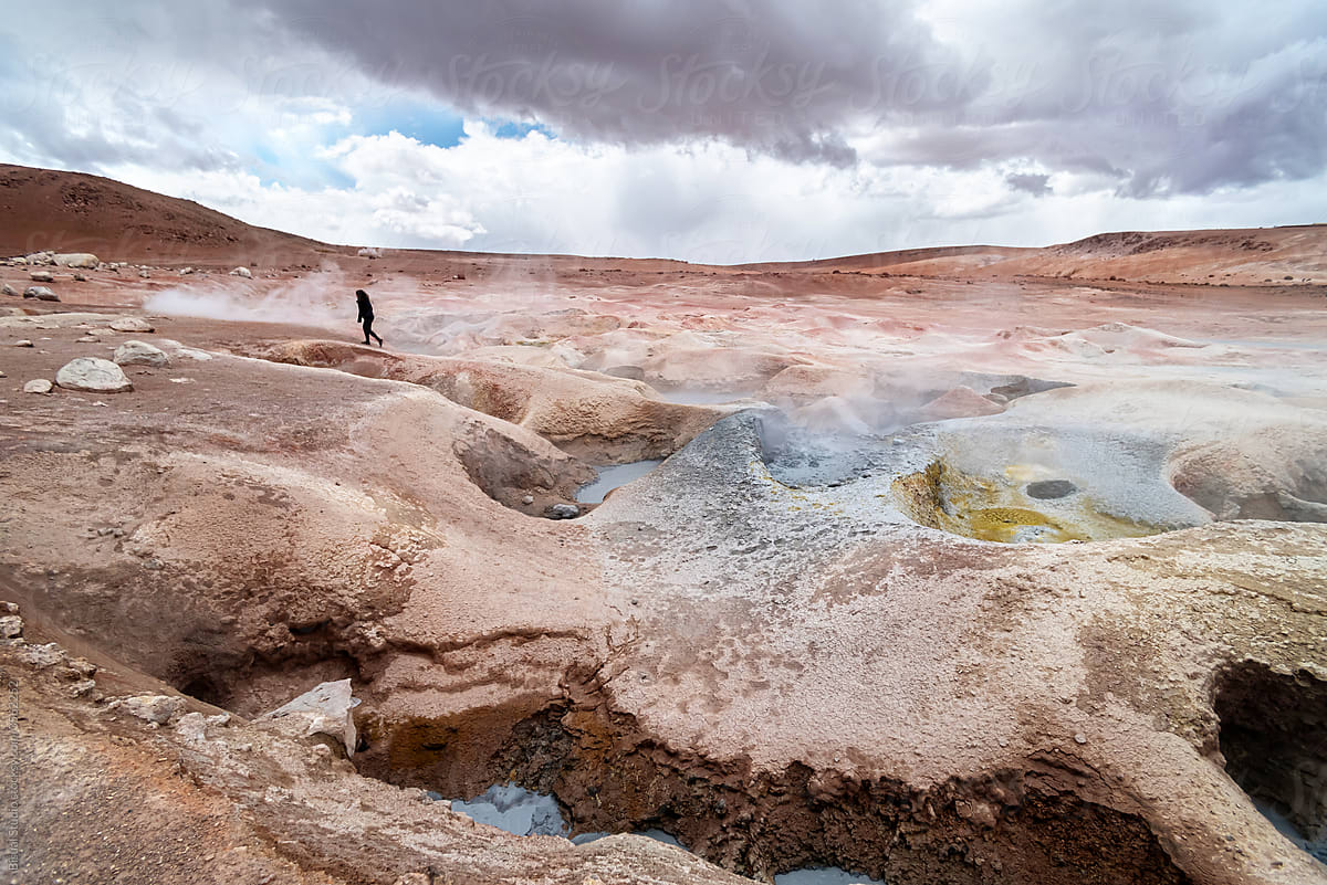 Woman walking through some geysers with volcanic activity and mud pits
