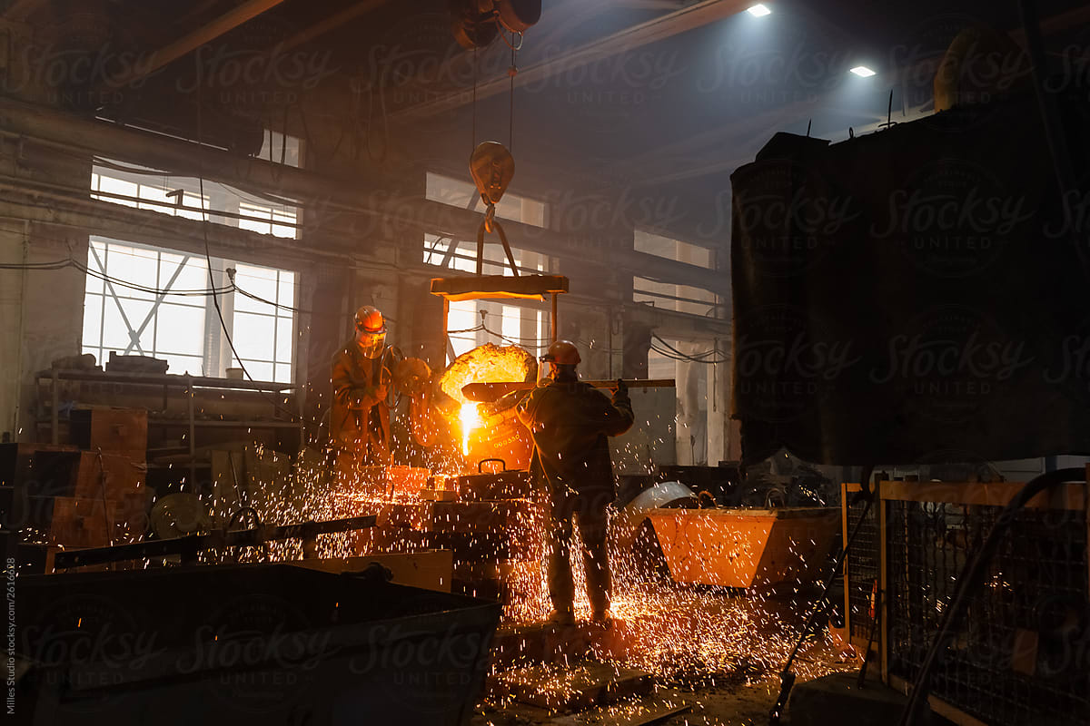 Men pouring sparkling metal in mold in foundry