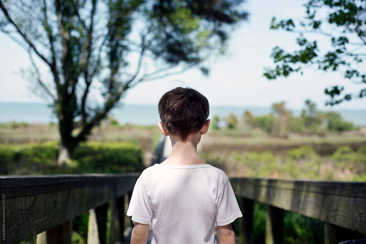 Boy stands at the top of a ramp, looking out to the ocean