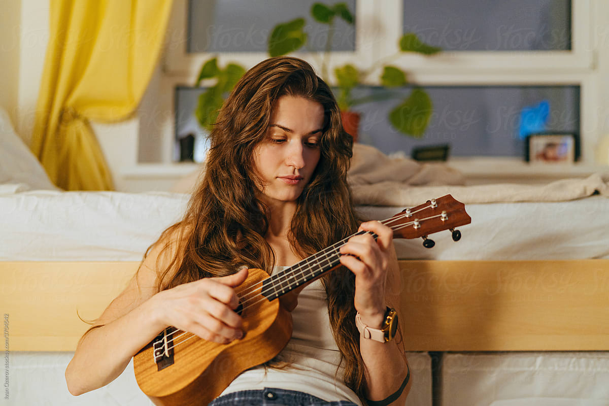 young woman playing ukulele in her room in the evening