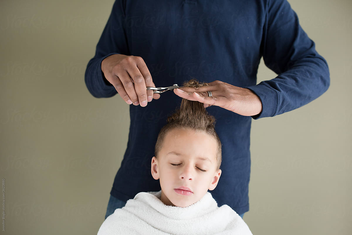 Boy closes eyes as father trims hair