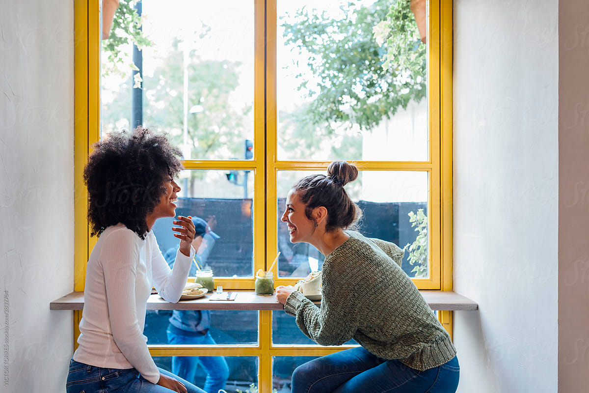 Multiracial women laughing near cafe window