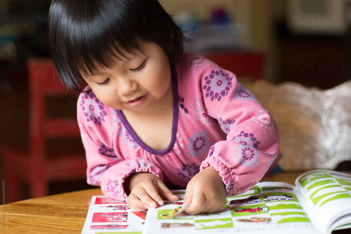 Girl playing with a sticker book at a dining room table