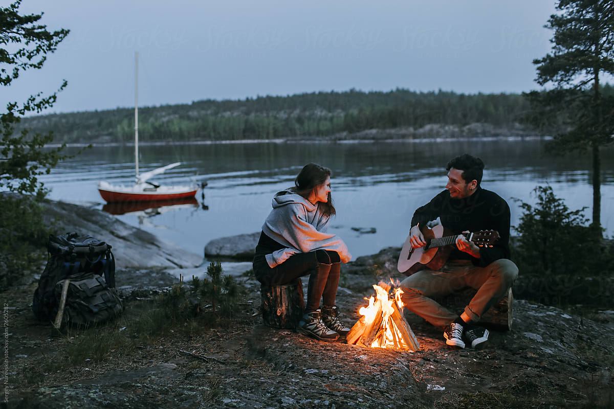 Traveling couple sitting around campfire on lake shore