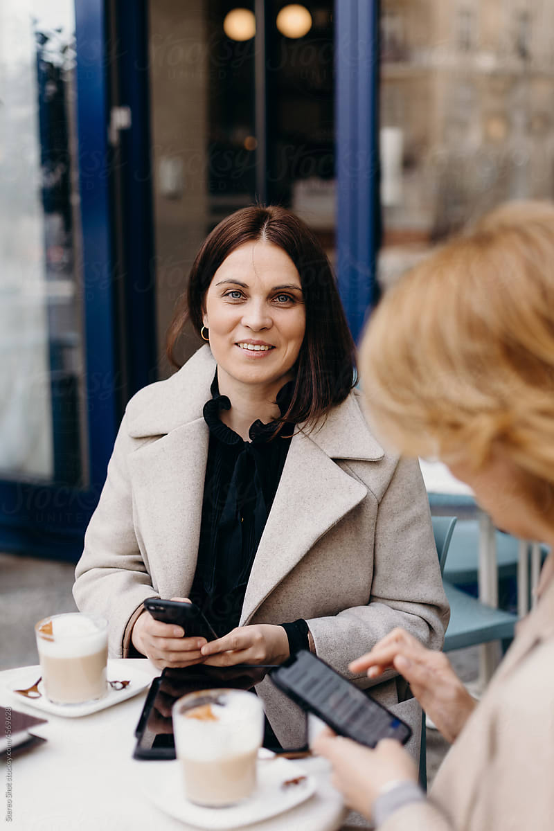 Smiling woman using smartphone near colleague in cafe