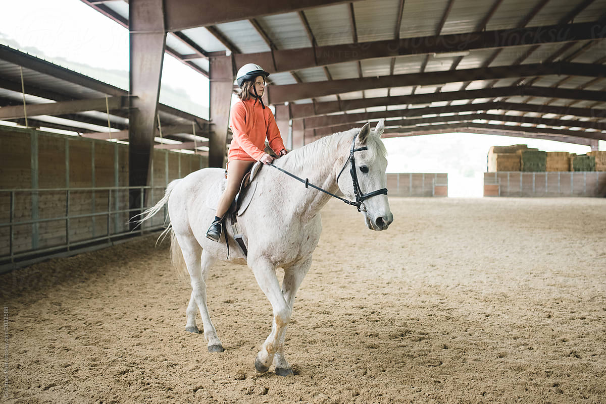 Adolescent rides horse in arena.