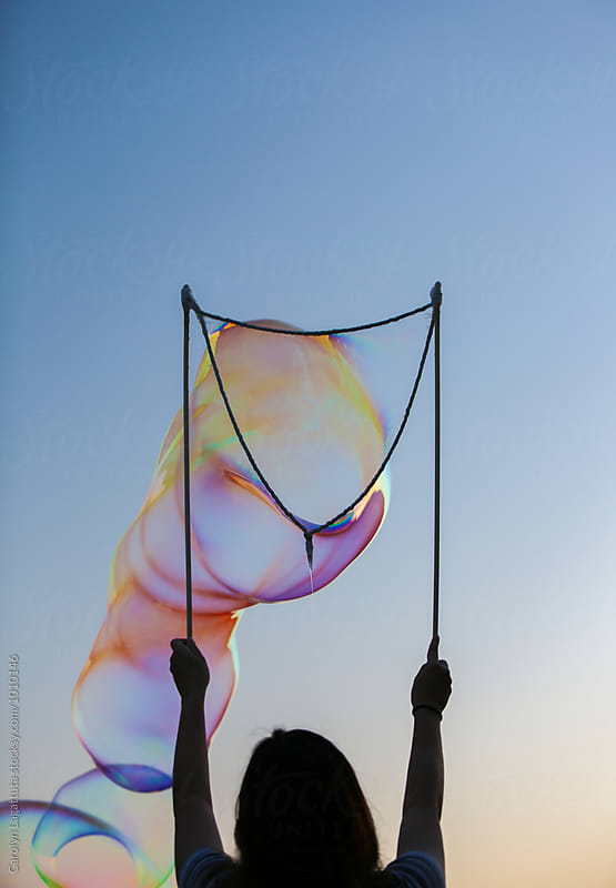 Person holding up sticks to form soap bubbles at sunset