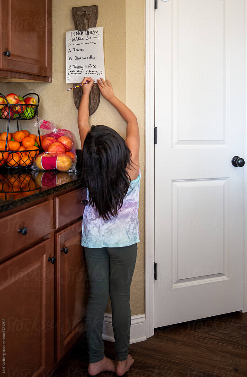 Full body view of girl marking choices on lunch menu in a home kitchen