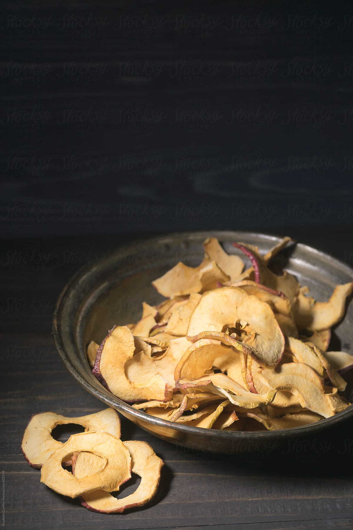 Dried apple chips in vintage pewter plate in dark moody light