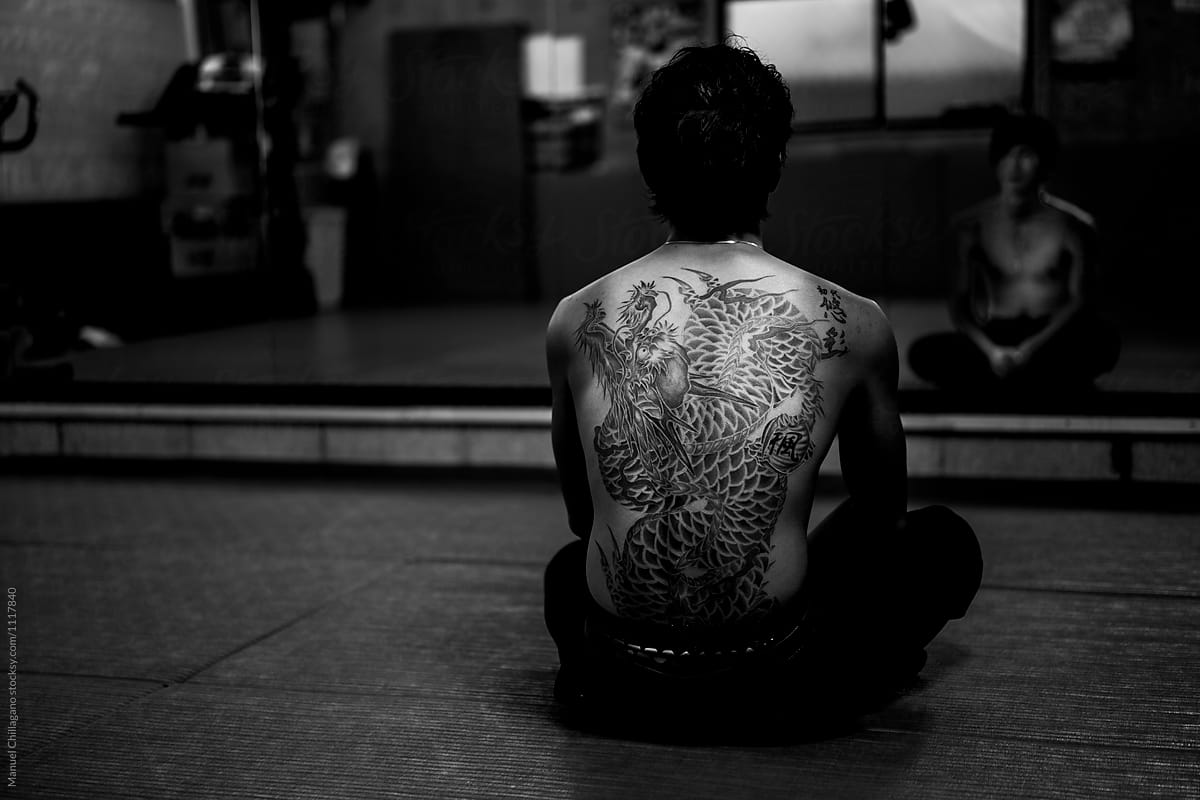 Black and white portrait of a heavily tattooed Japanese man watching himself in a big mirror