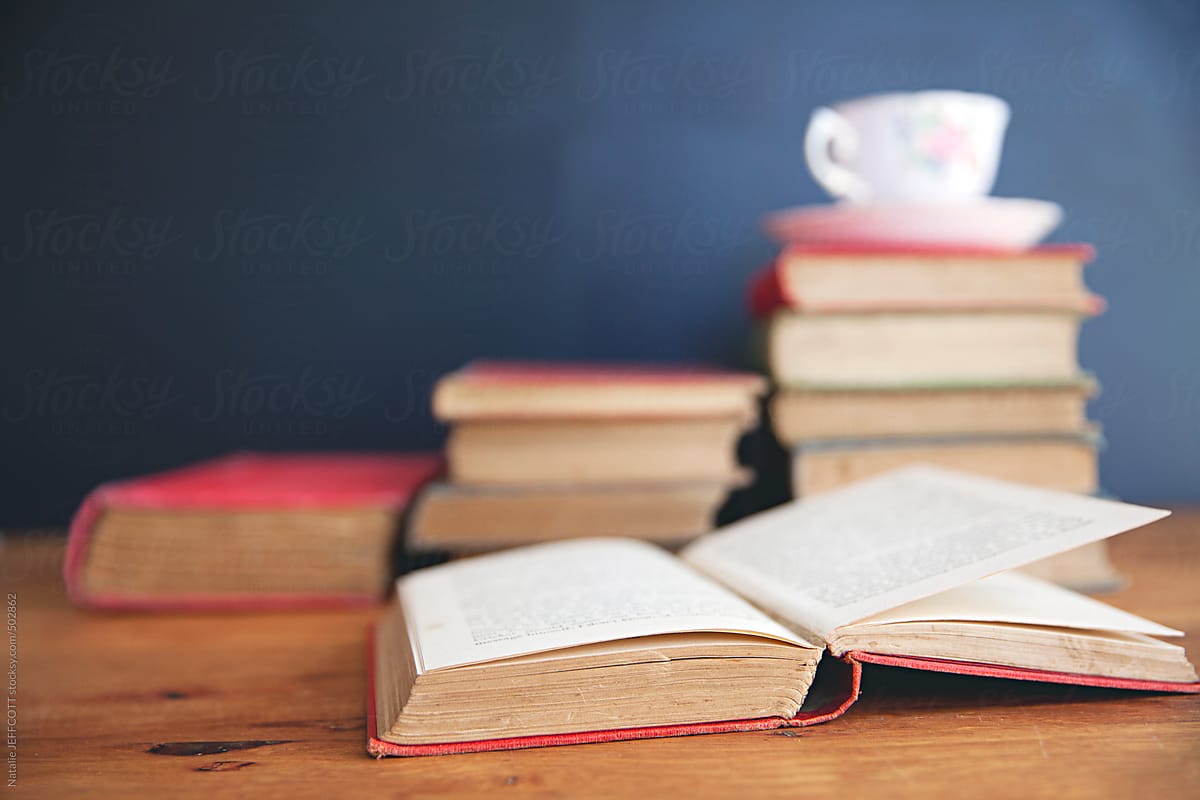 an open book on top of a pile of books with cup