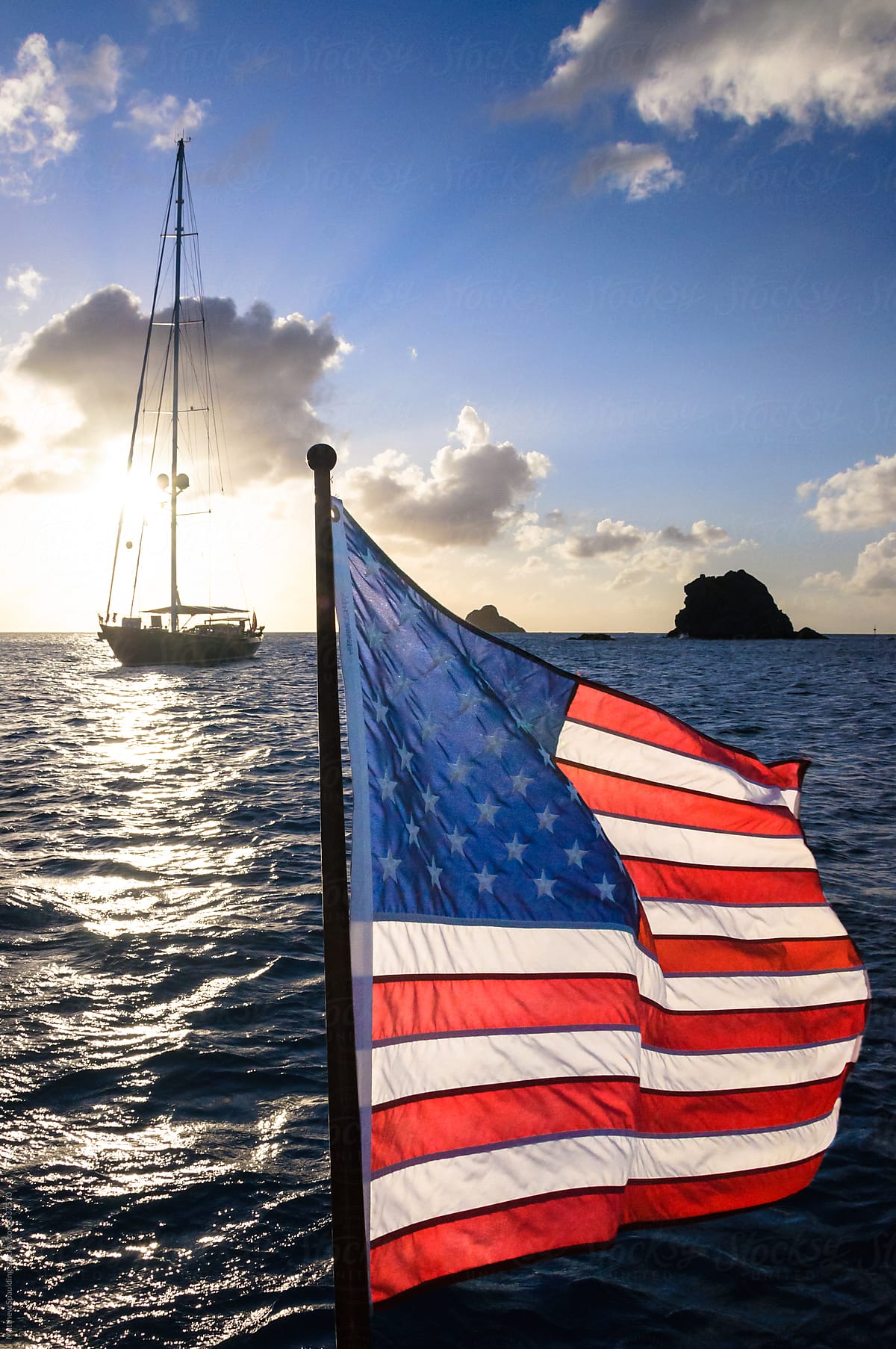 American flag flying in wind with sailboat on ocean during summer sunset