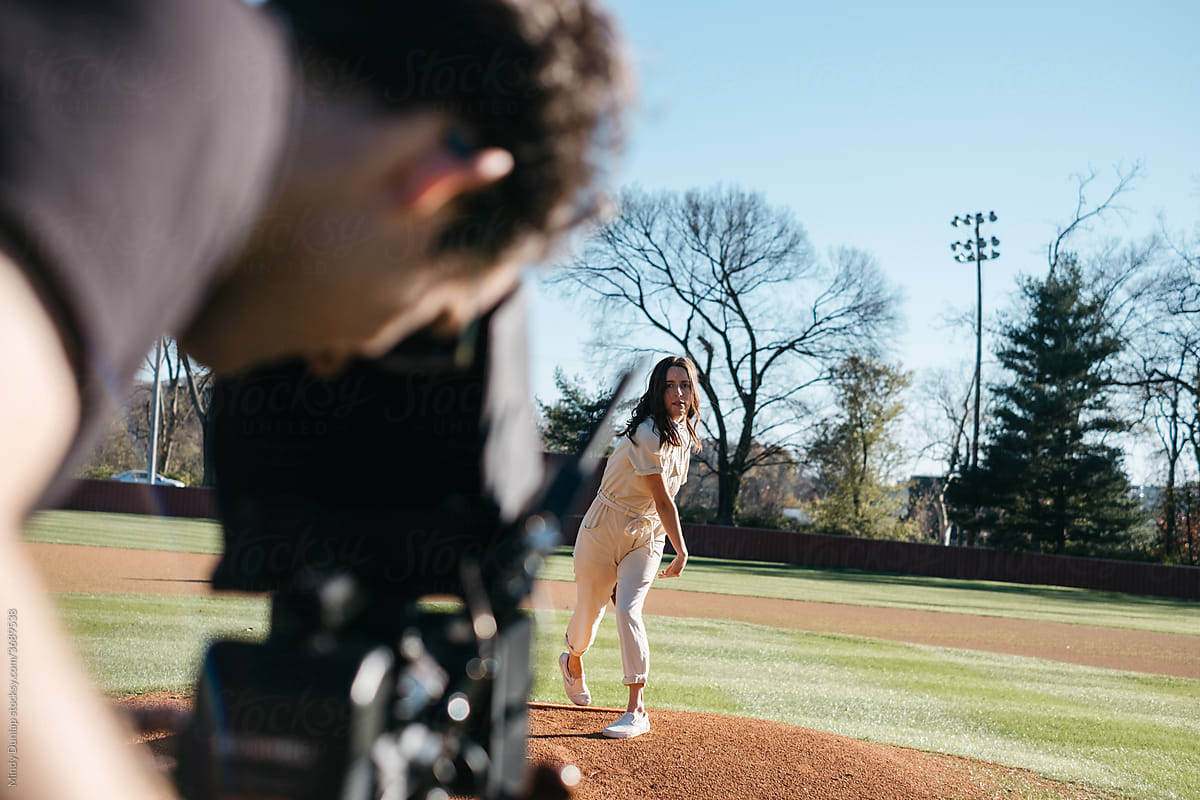 Cinematographer filming a female pitcher on a baseball field