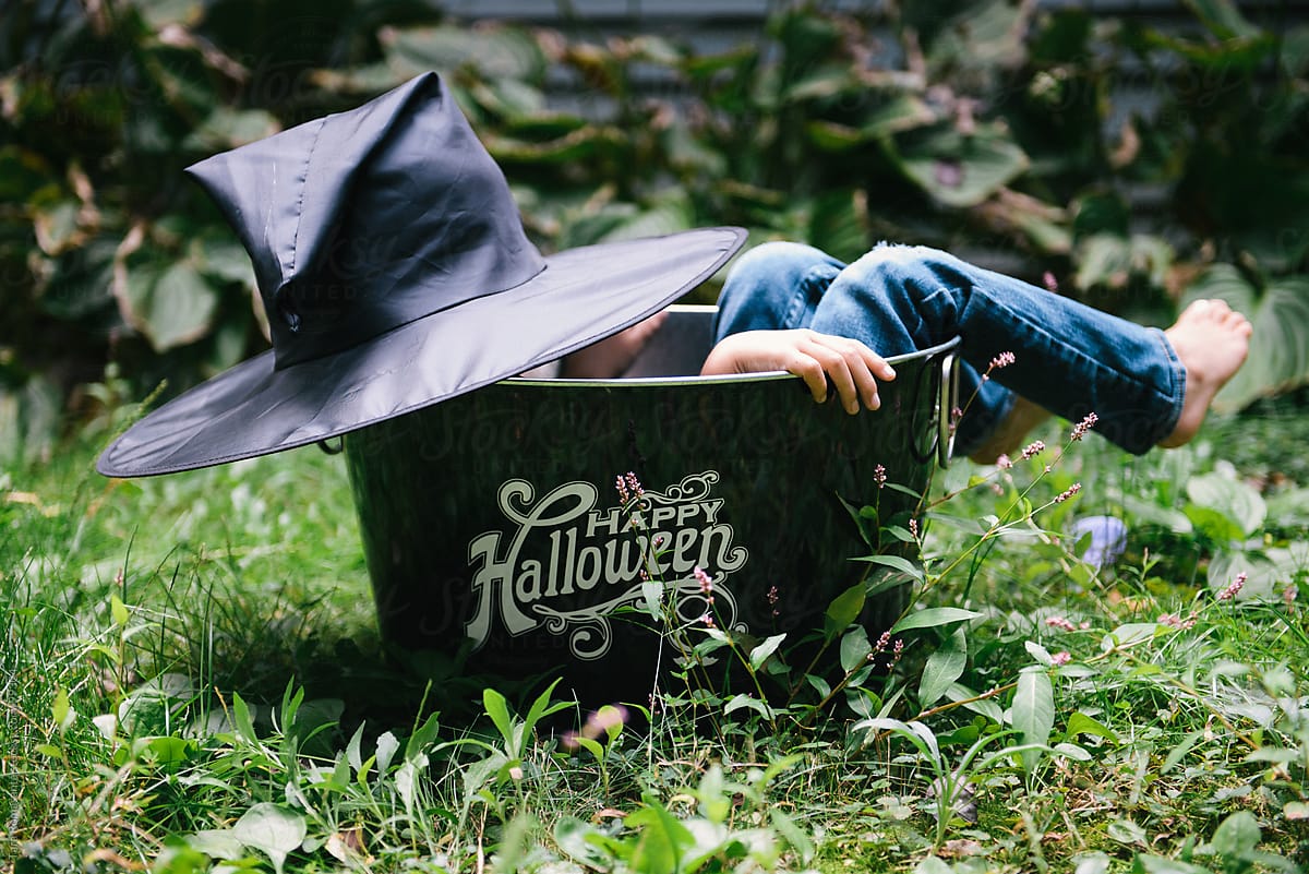child in witch hat costume hides in a Halloween decoration