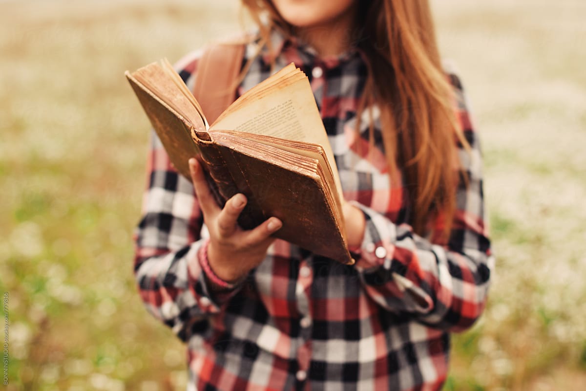 Closeup of a 14 years old girl reading an old book in a rural landscape.