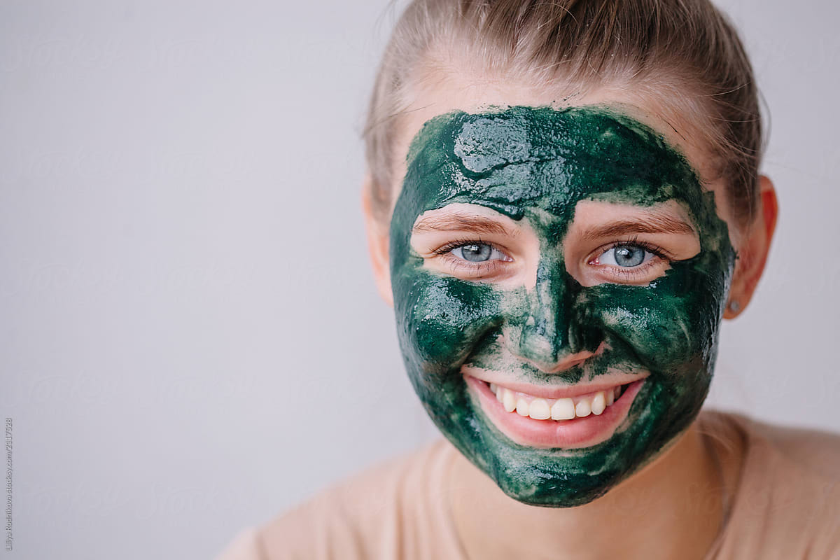 Lovely blond female with green skincare mask on her face
