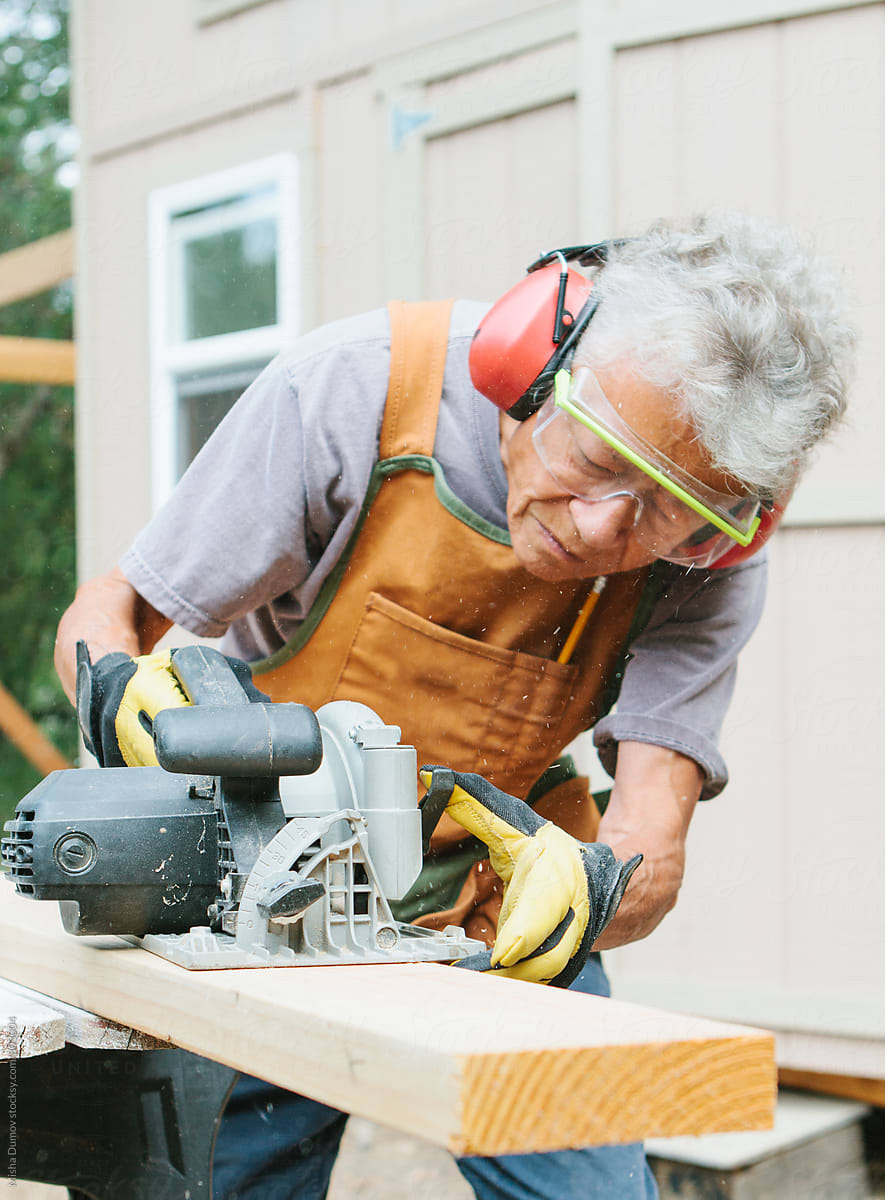 Elderly woman carpenter using circular hand saw to cut lumber