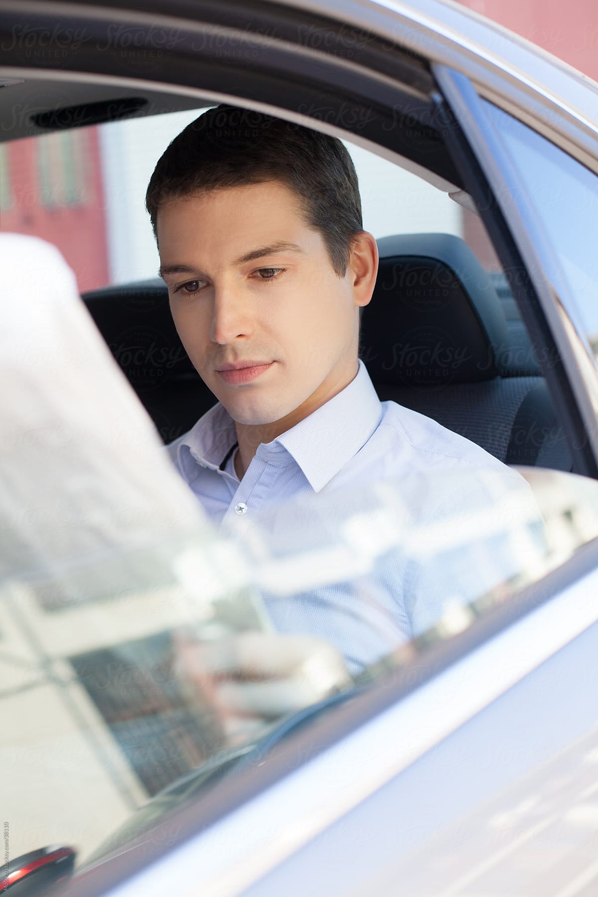 Businessman sitting in a backseat of the car and reading newspapers.