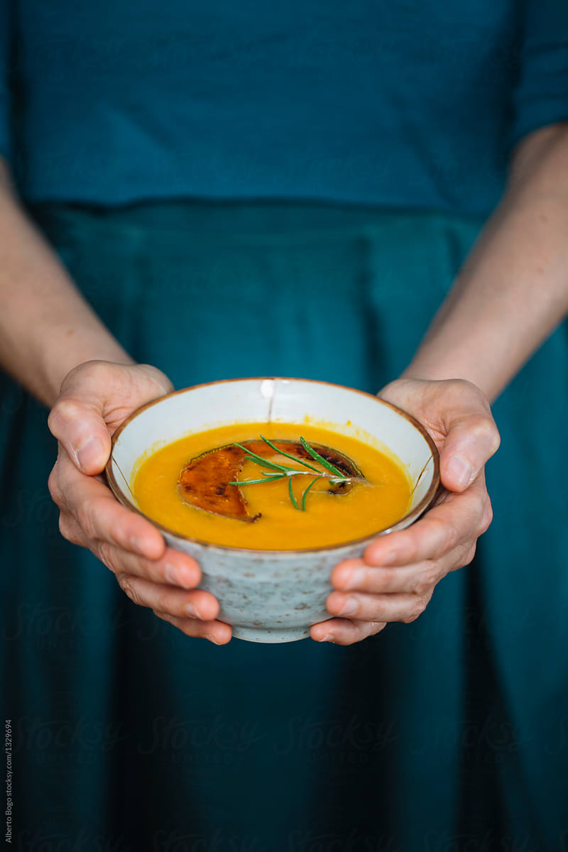 Person holding pumpkin soup bowl