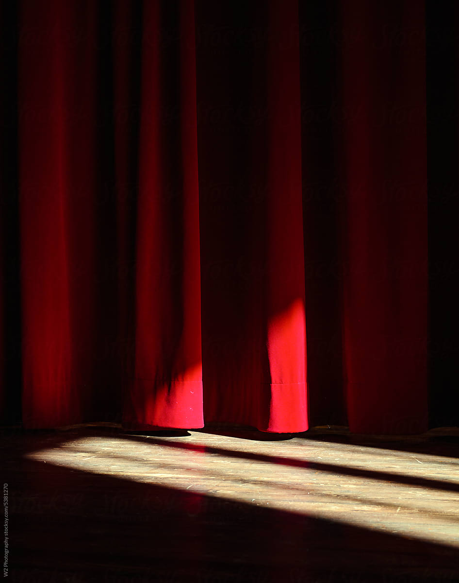 A sun beam on a wood floor and red stage curtain.