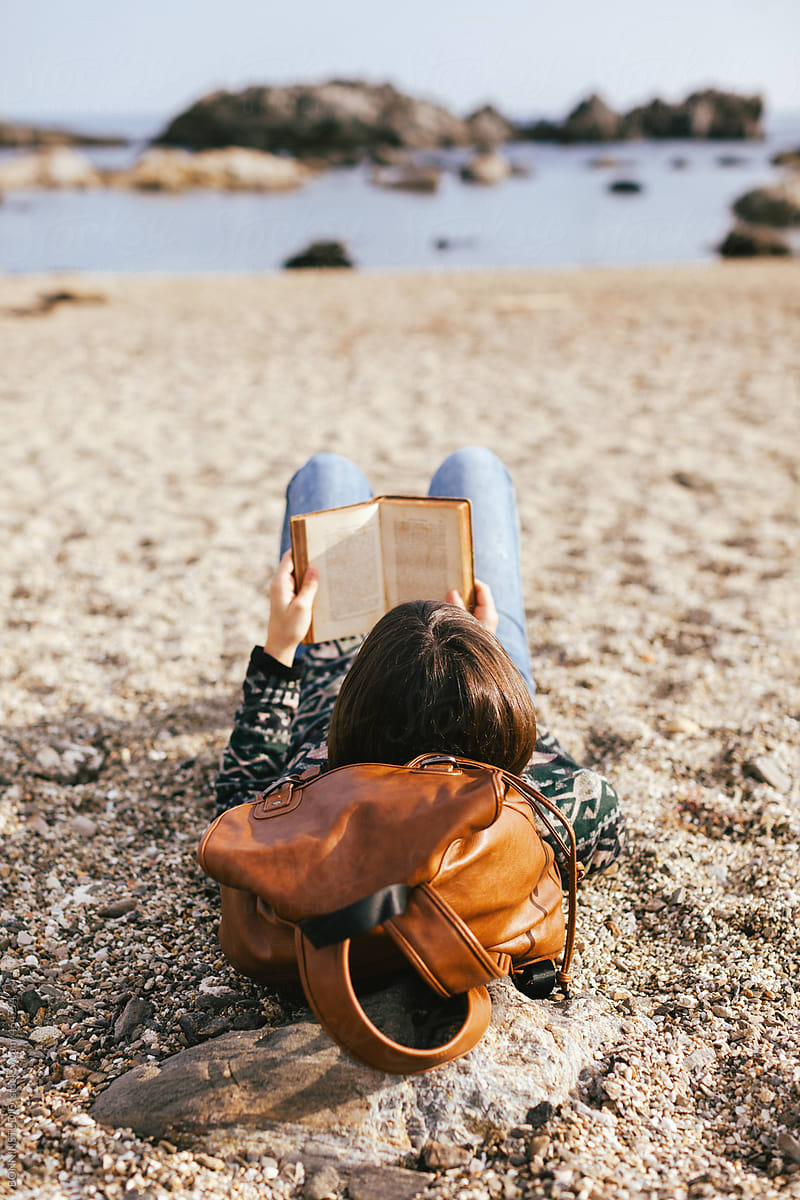 Back view of woman relaxing reading a book on the beach.