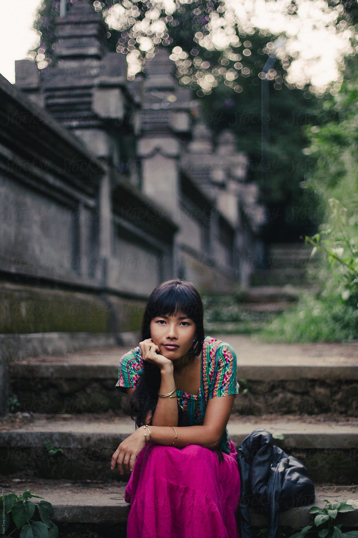 Beautiful young Asian woman in pink skirt sitting by the temple stone wall