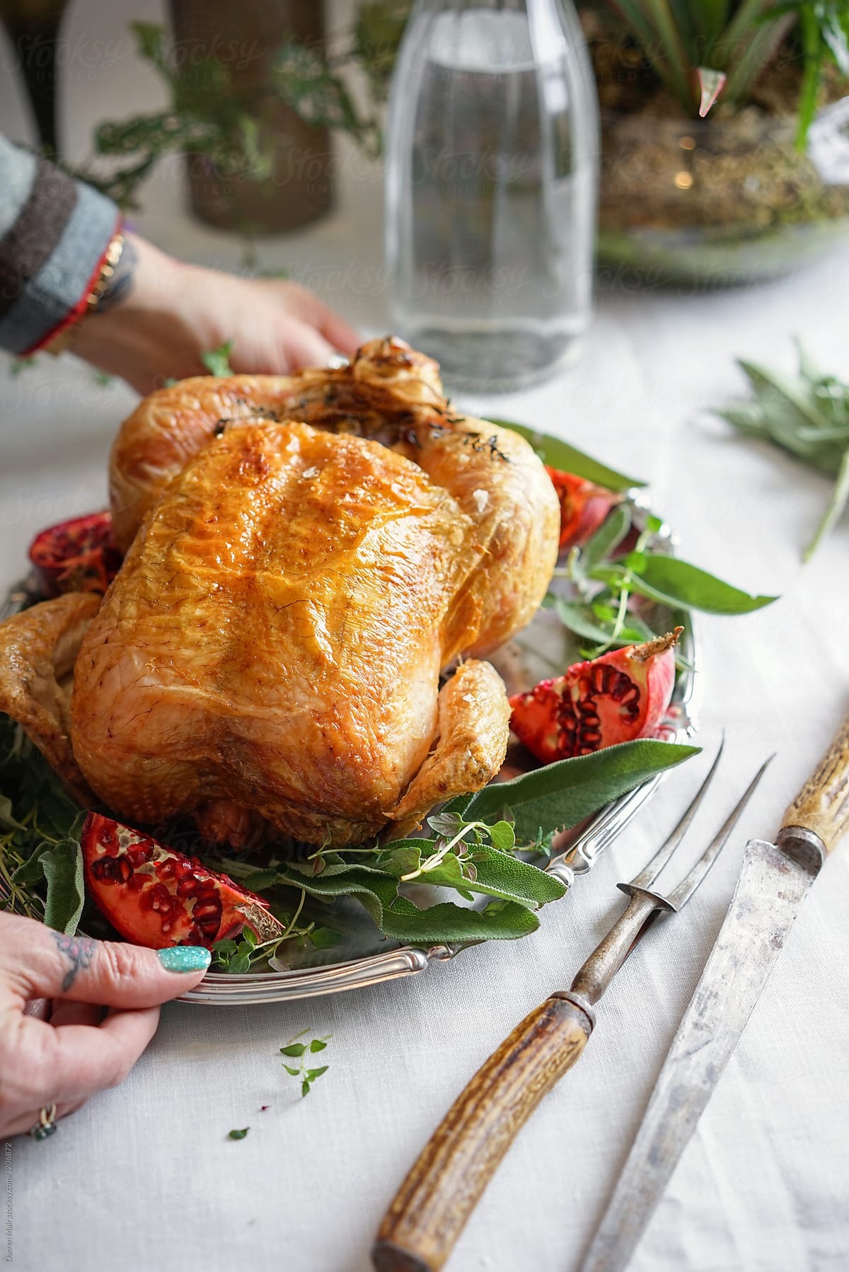 Whole roast chicken with herbs and pomegranate on a silver,being served onto a table.