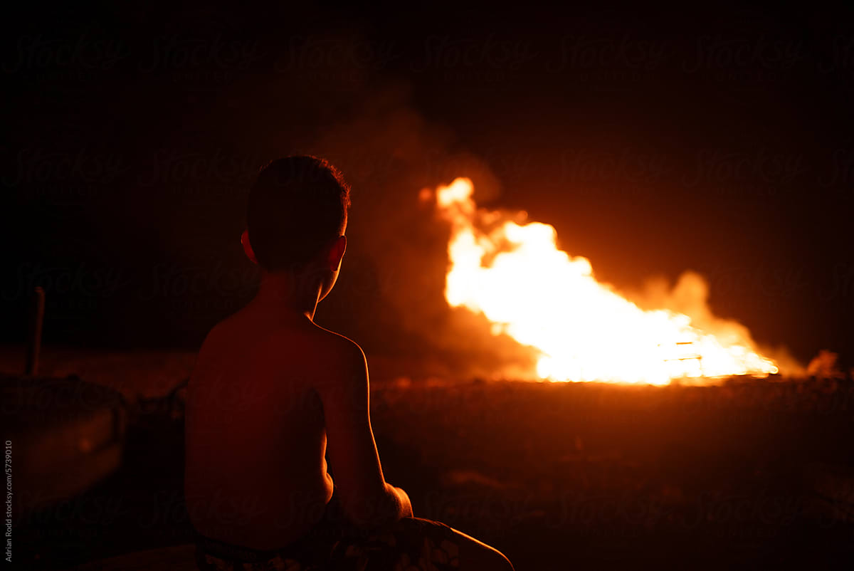 A teenager stares at a controlled fire at night