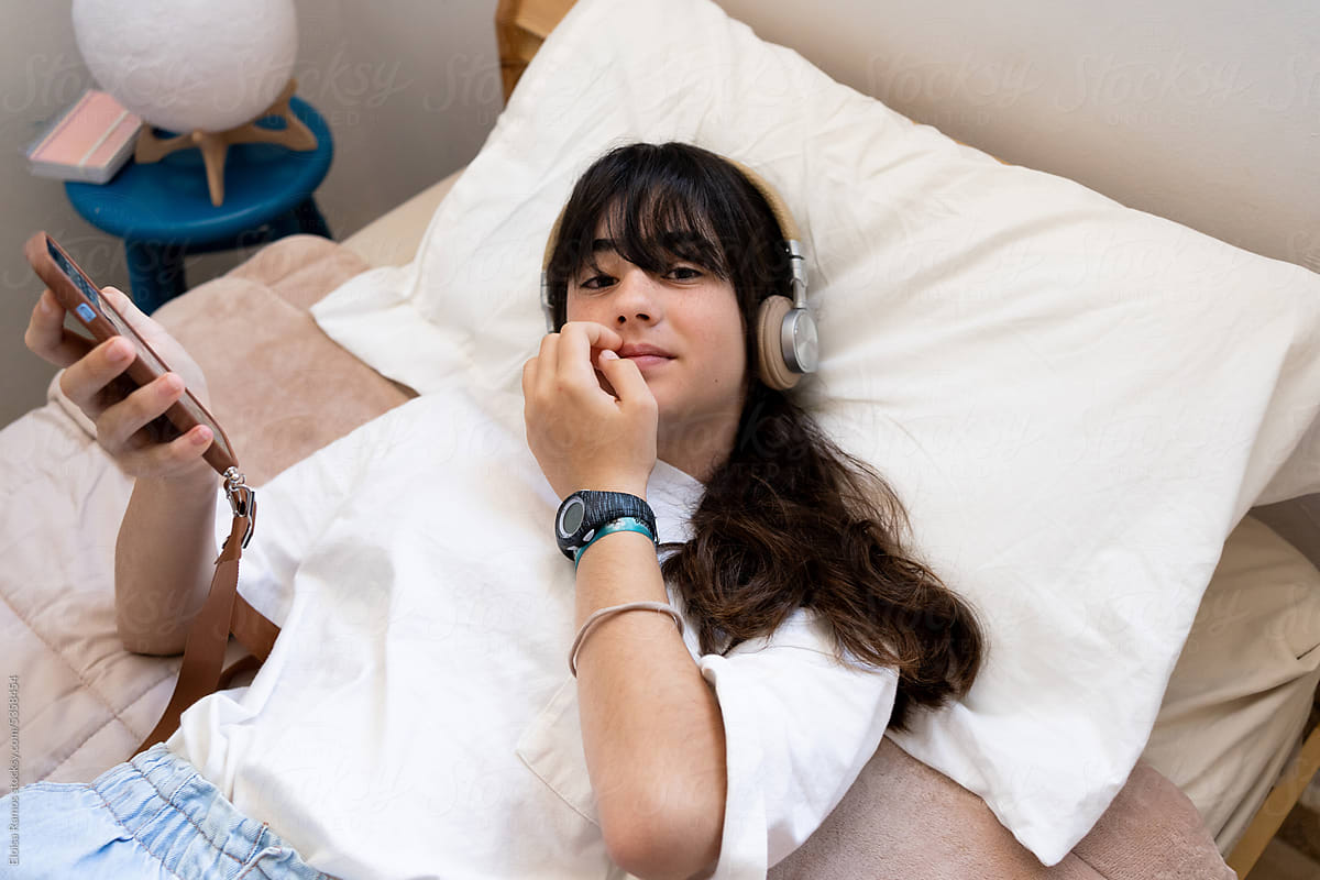 Teen Girl Chilling With Smartphone and headphones On Bed