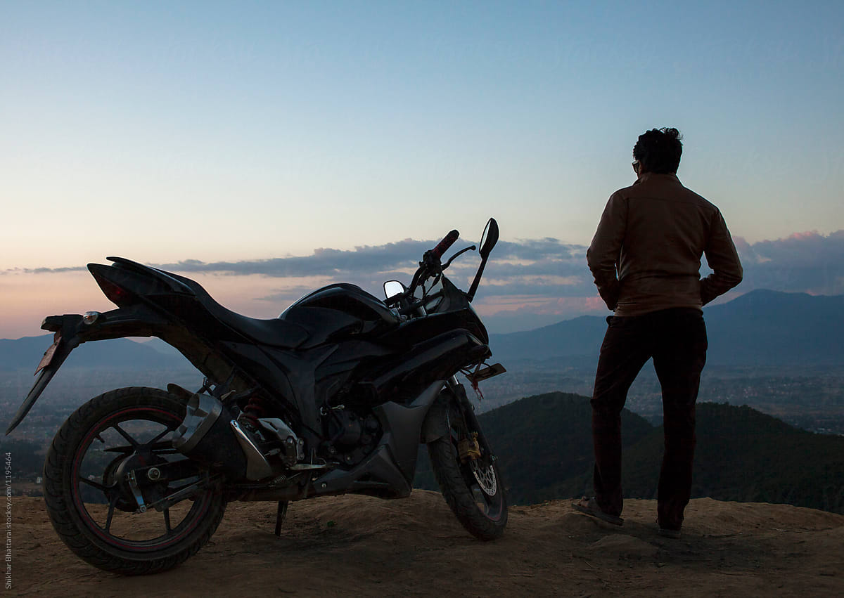 A silhouette of a man and his motorbike on top of a hill.