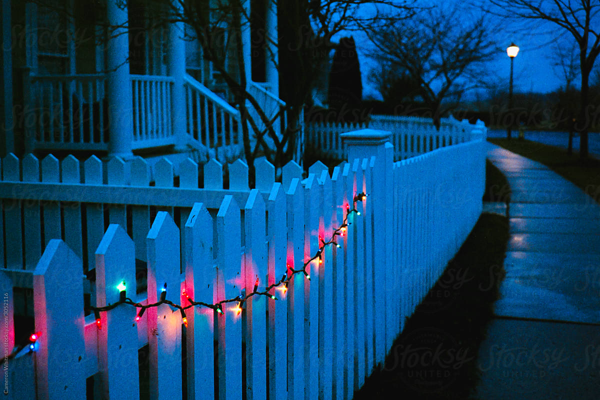 String of Christmas lights hung on a white picket fence