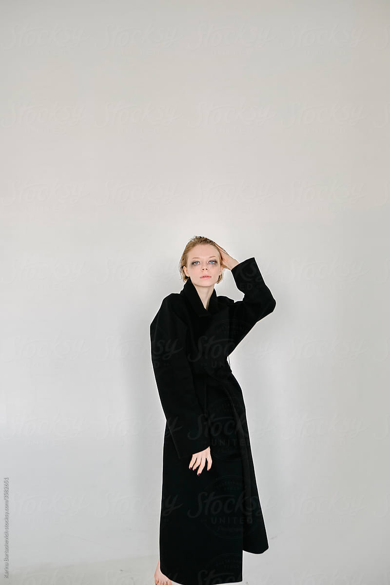 art portrait of a beautiful girl in a black coat on a white wall background