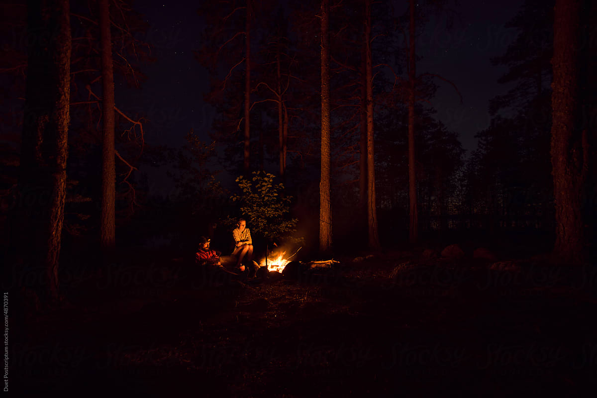 Friends near bonfire in camping zone in the forest.