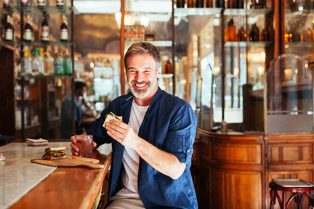 Cheerful man enjoying sandwich and drink in bar