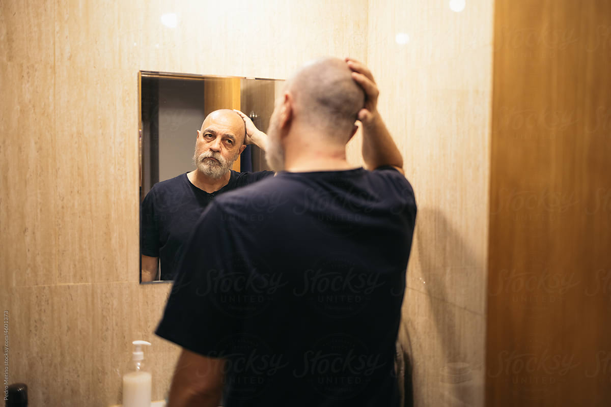 Middle-aged bearded man looking in the mirror