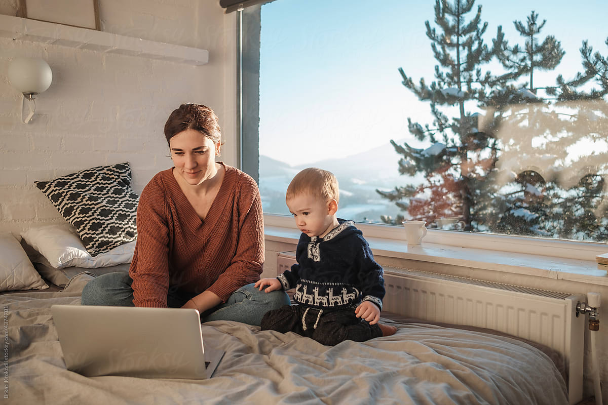 Mother And Baby Sitting On The Bed With Laptop