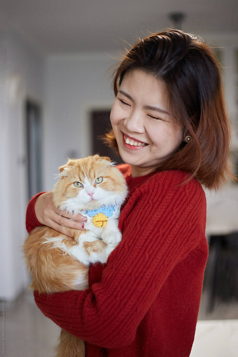 Young Chinese Woman Smiles As She Holds Her Cat At Home