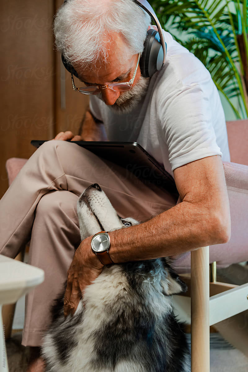 Elder gentleman petting Husky at home.