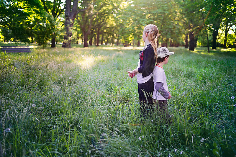 Boy and girl standing back to back in long grass in a park