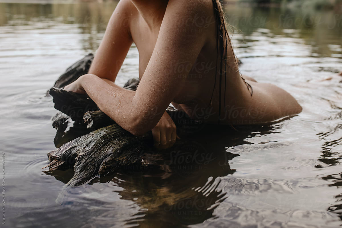 Anonymous naked woman leaning over the tree in pond lake water