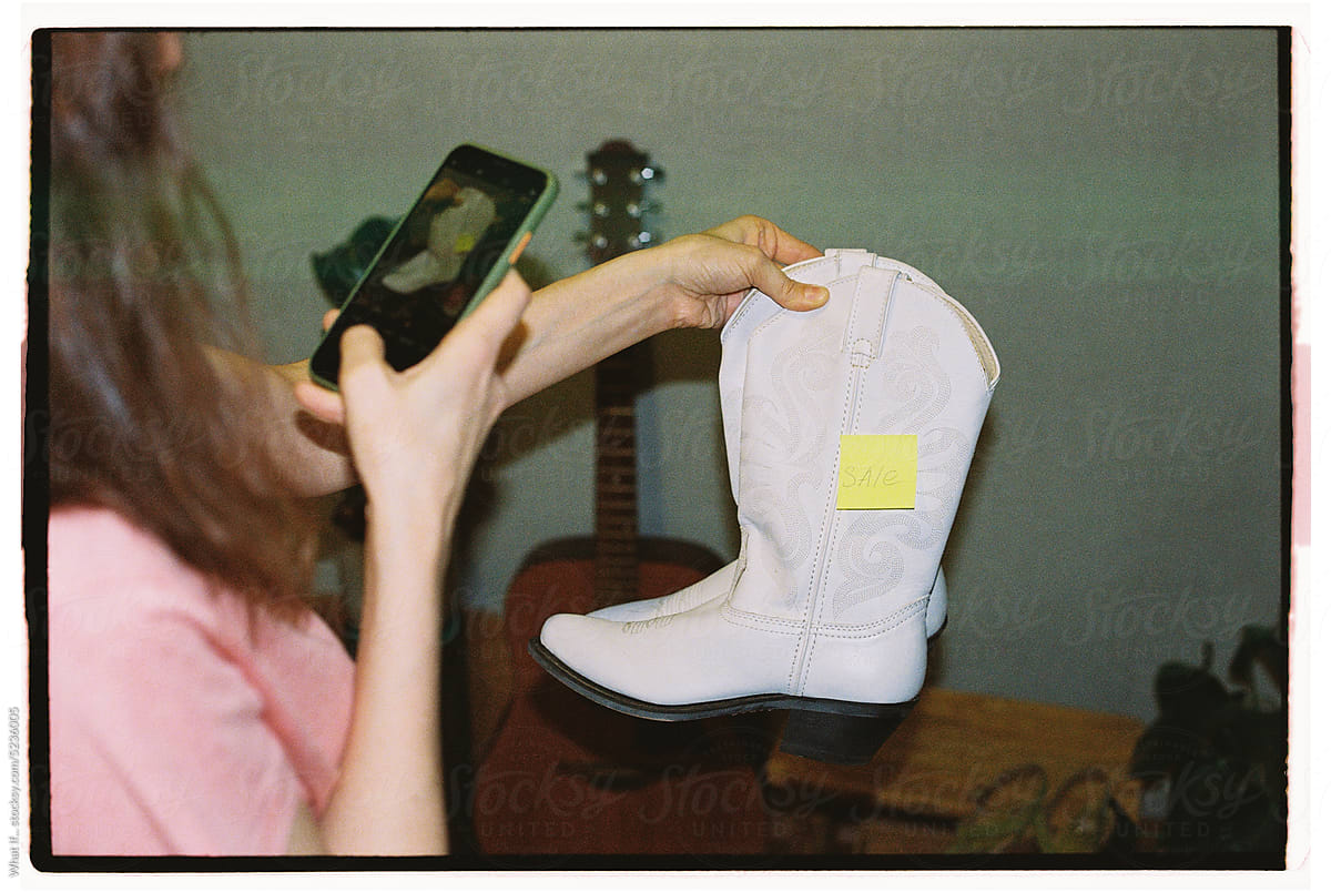 Woman taking pictures of stylish cowboy boots at a flea market.