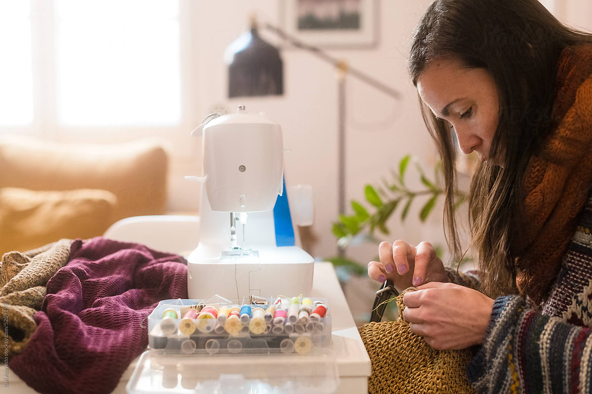 Focused woman sewing and fixing handbag at home