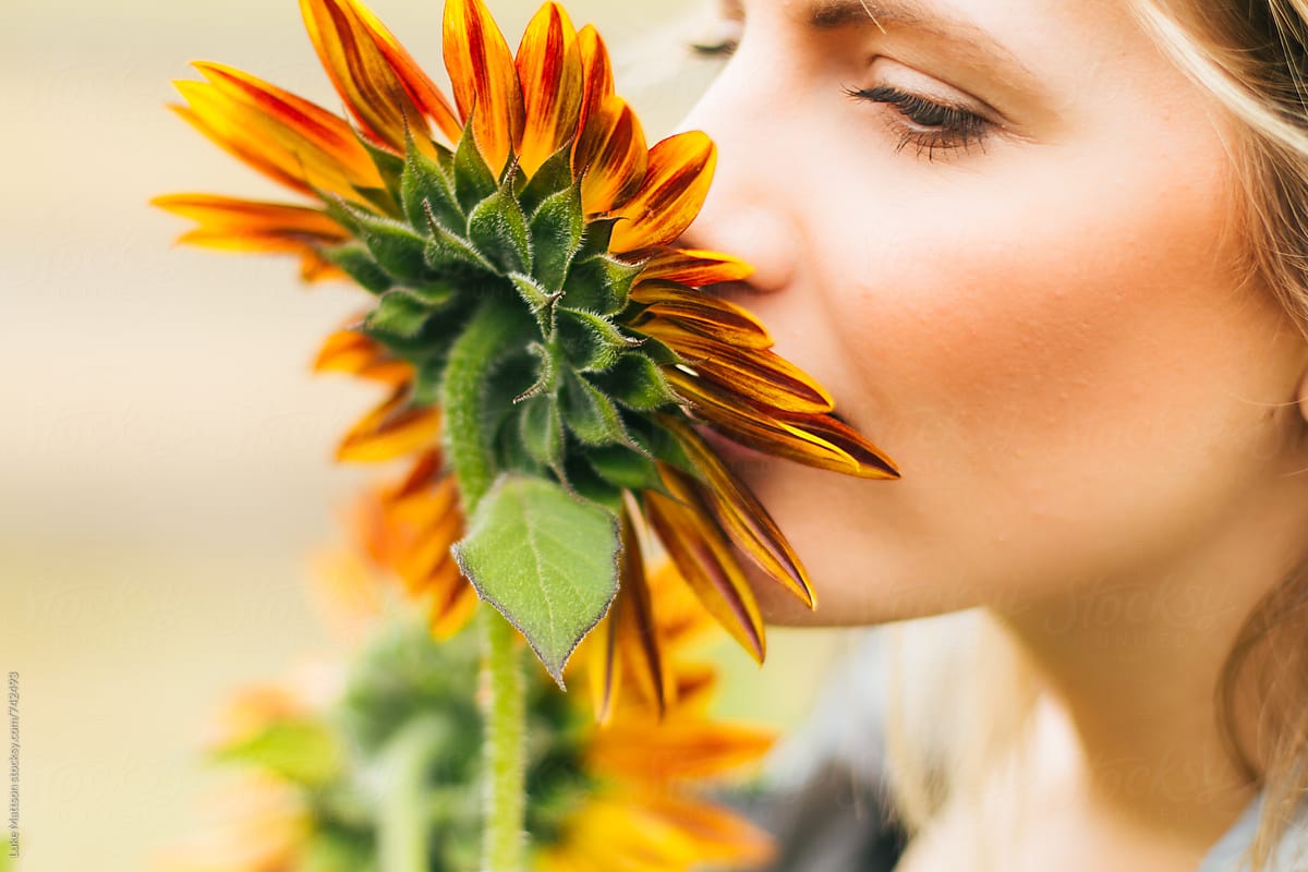Young Blonde Woman Smelling A Red Sunflower